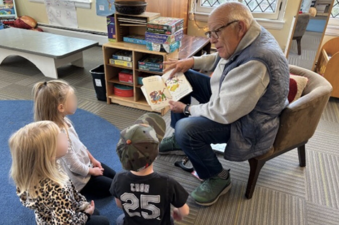"Grandpa Jim" reads a book to three young children in a classroom.