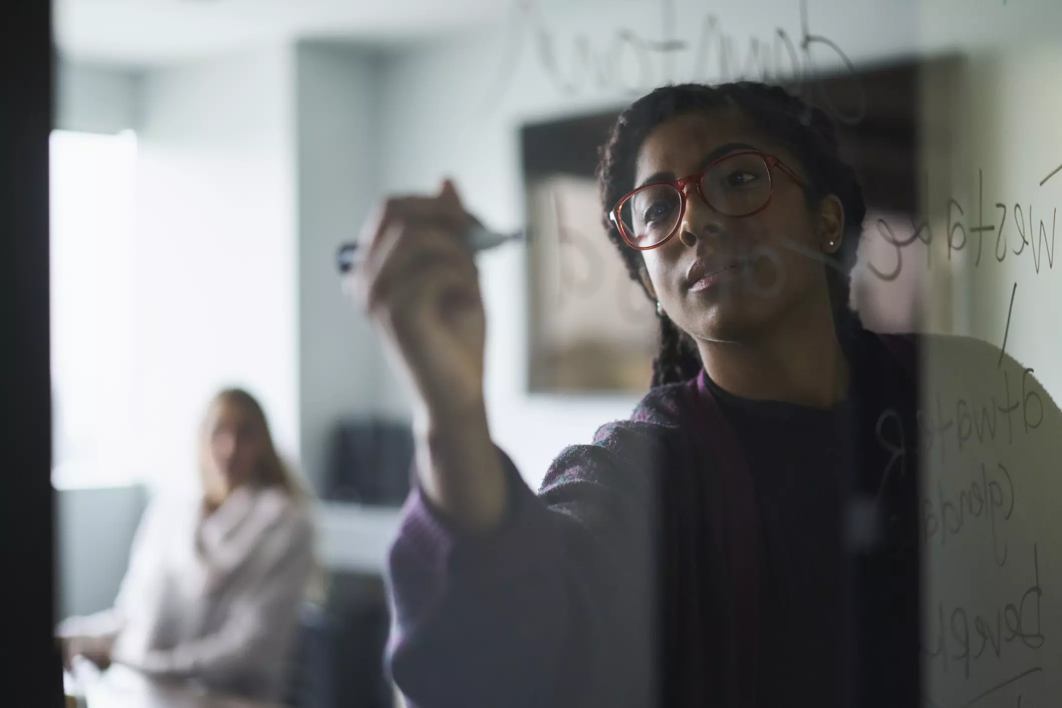woman of color writing on a transparent whiteboard