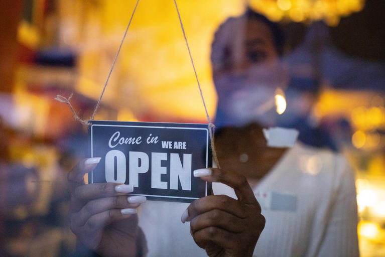 Photo of new business owner placing Now Open sign in window